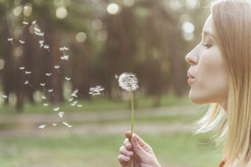 tranquil woman standing in park and blowing on dandelion. Copy space in left side