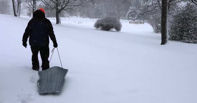 Man pulling sled up hill outdoor on snowy winter afternoon.