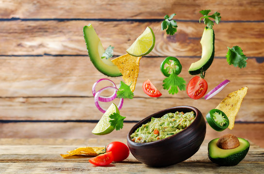 Guacamole with flying corn chips and ingredients to prepare it