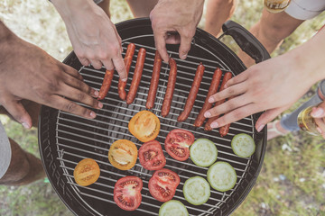 male and female hands taking grilled sausages and vegies from barbecue. Top view close up