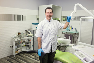 Male dentist standing over medical office background. Healthcare, profession, stomatology and medicine concept