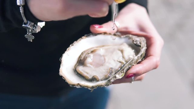 Close-up shot of women pouring lemon juice on the open oysters at the street. Delicious seafood in hand, Dynamic Slow motion