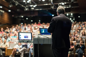 Speaker giving a talk on corporate business conference. Unrecognizable people in audience at...