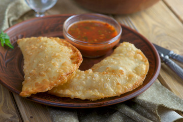 chebureks with tomato sauce on wooden background