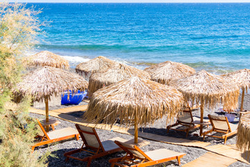 beach with umbrellas and deck chairs by the sea in Santorini