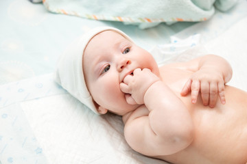 A naked baby in a white cap lies on the bed.