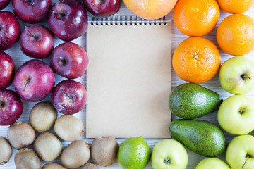 Set of raw fruits with notebook on white wooden background. Top view. Flat lay.