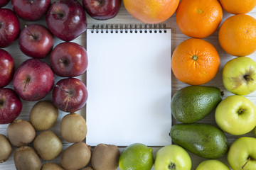 Set of raw fruits with notebook on white wooden background. Top view. Flat lay.