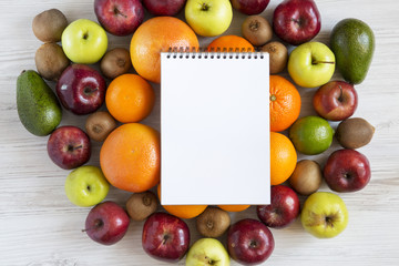Set of raw fruits with notebook on white wooden background. Top view. Flat lay.