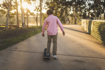 Rear view of boy skateboarding on footpath at park during sunset