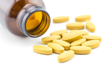 Pills of vitamin C spilled out open container on white background.