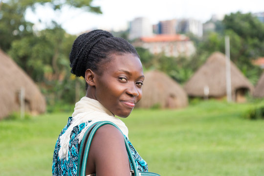 A beautiful smiling young Ugandan woman with thatched roundhouses in the background