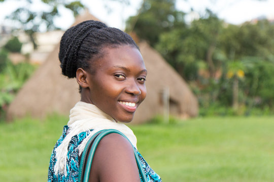 A beautiful smiling young Ugandan woman with thatched roundhouses in the background
