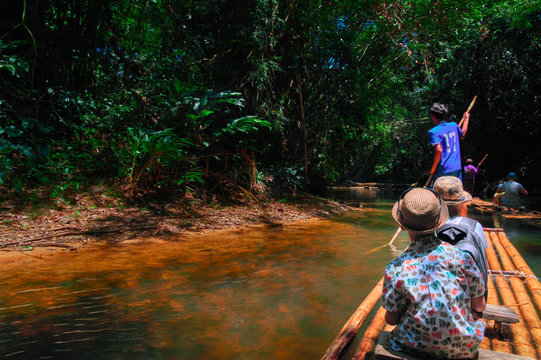 Boys (8 years old) floating along tropical river on bamboo raft in jungle. Concept traveling with children back view. Copy space.