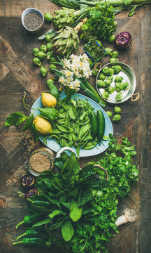 Spring healthy vegan food cooking ingredients. Flat-lay of vegetables, fruit, seeds, sprouts, flowers, greens over wooden background, top view, vertical composition. Diet, clean eating food concept
