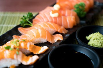 Mixed salmon sushi on black plate along with Japanese sauce and green leaf decoration, Japanese food, close up at sushi ..