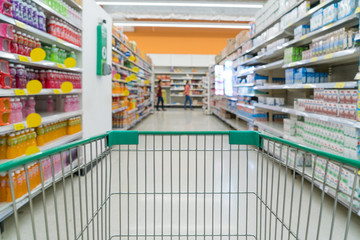 Abstract blurred photo of store with trolley in department store bokeh background. Supermarket aisle with empty green shopping cart.
