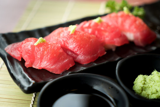 Tuna sushi on black plate along with Japanese sauce and green leaf decoration, Japanese food, close up at sushi ..