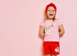 Cute baby girl kid in light pink pajamas and red headband happy smiling on pink