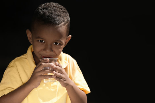 African American child drinking water on dark background. Water scarcity concept