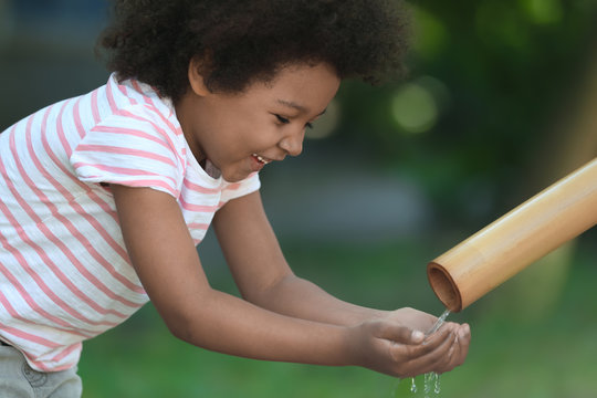 African American child drinking water from pipe outdoors. Water scarcity concept