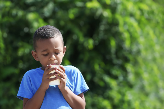 Cute African American boy drinking water from plastic cup, outdoors