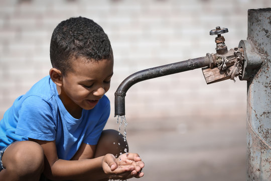 African American boy drinking water from tap, outdoors