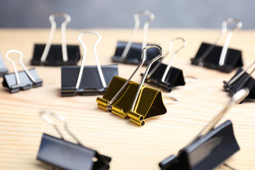 One golden binder clip among black ones on wooden table. Difference and uniqueness concept