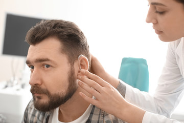 Obraz na płótnie Canvas Otolaryngologist putting hearing aid in man's ear in hospital