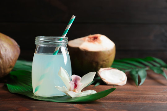 Glass jar of coconut water and beautiful flower on wooden table