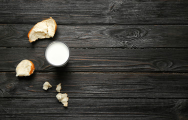 Obraz na płótnie Canvas Glass of milk and bun pieces on wooden background, top view