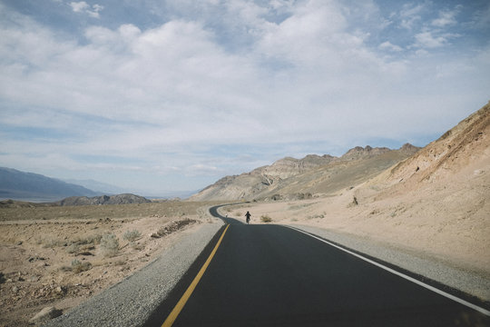 Distant view of father and son riding bicycles on desert road against cloudy sky