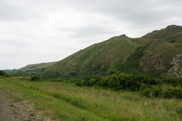 Fototapeta premium Unique green mountain landscape with high rocky mountains and cloudy sky on background and part of dirty road on foreground.