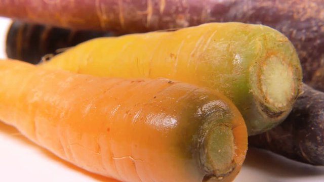 A bunch of carrots (not the usual variety, yellow and violet colors) on a rotating surface. Front close-up shot.
