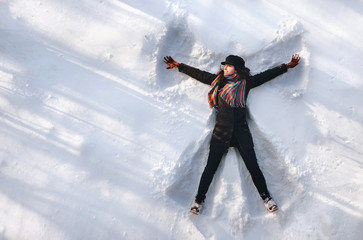 A girl on the snow shows an angel. Spreading arms. Top view. Drone. Smile. Happy.