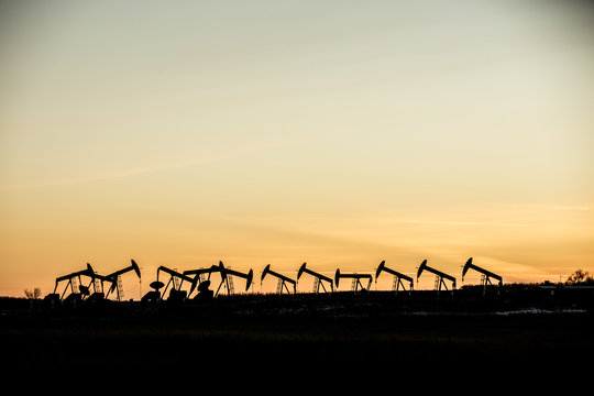 Mid distance view of silhouette pumpjacks at oil industry against sky during sunset
