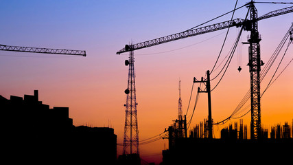 silhouette of building under construction with crane at sunset