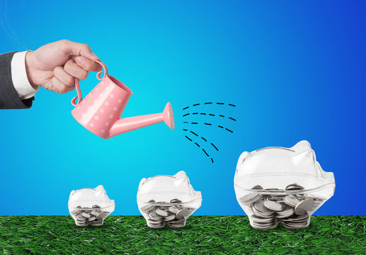 Transparent piggy bank filled with coins on wood background.Saving investment colorful concept.Watering can and money growth drawn concept for business investment, savings and making money.