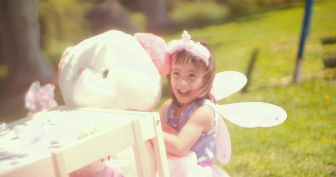 Little girl in fairy costume hugging teddy bear in garden
