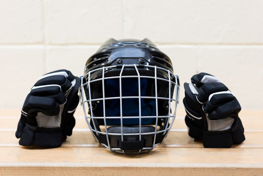 Kid's Hockey Gear On The Bench: Black Hockey Helmet And Gloves. 