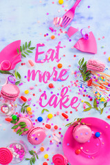 Party concept with Eat more cake paper text, candies, sweets, confetti and macarons. Colorful Birthday celebration flat lay.