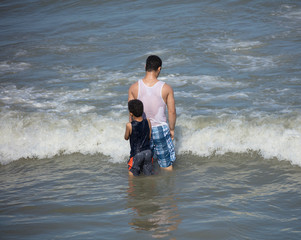 unknown boy hides from waves behind his unknown brother