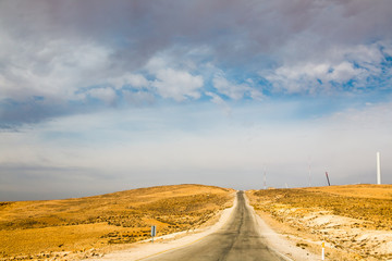 The road in the desert with yellow sand and clouds on the sky