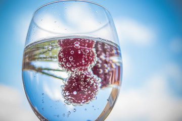 water with fresh fruits and glass dishware.cocktails with ripe sweet red cherry on blue sky background. Lemonade, summer drinks.Glass of lemonade ice water on blue sky background.