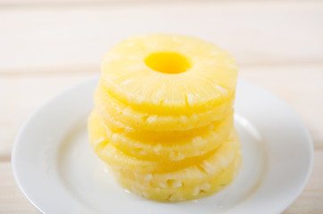 Pieces of pineapple. Pineapple chopped into round pieces in a pile on a white plate on a white wooden background
