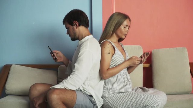 Young couple on couch turn away from each other use smartphone rapid slow motion