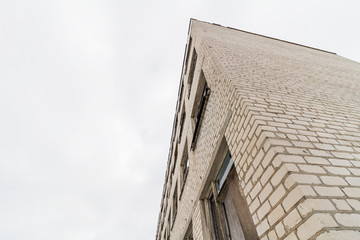 A part of abandoned dilapidated brick building with destroyed windows on the sky background