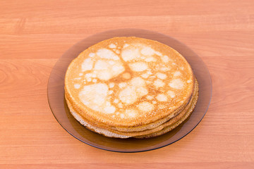 A glass plate of blini - traditional russian pancakes on the wooden table, top view