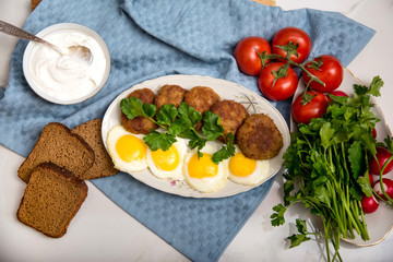 Meatballs and eggs with tomato, bread and greens
