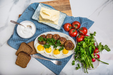 Meatballs and eggs with tomato, bread and greens